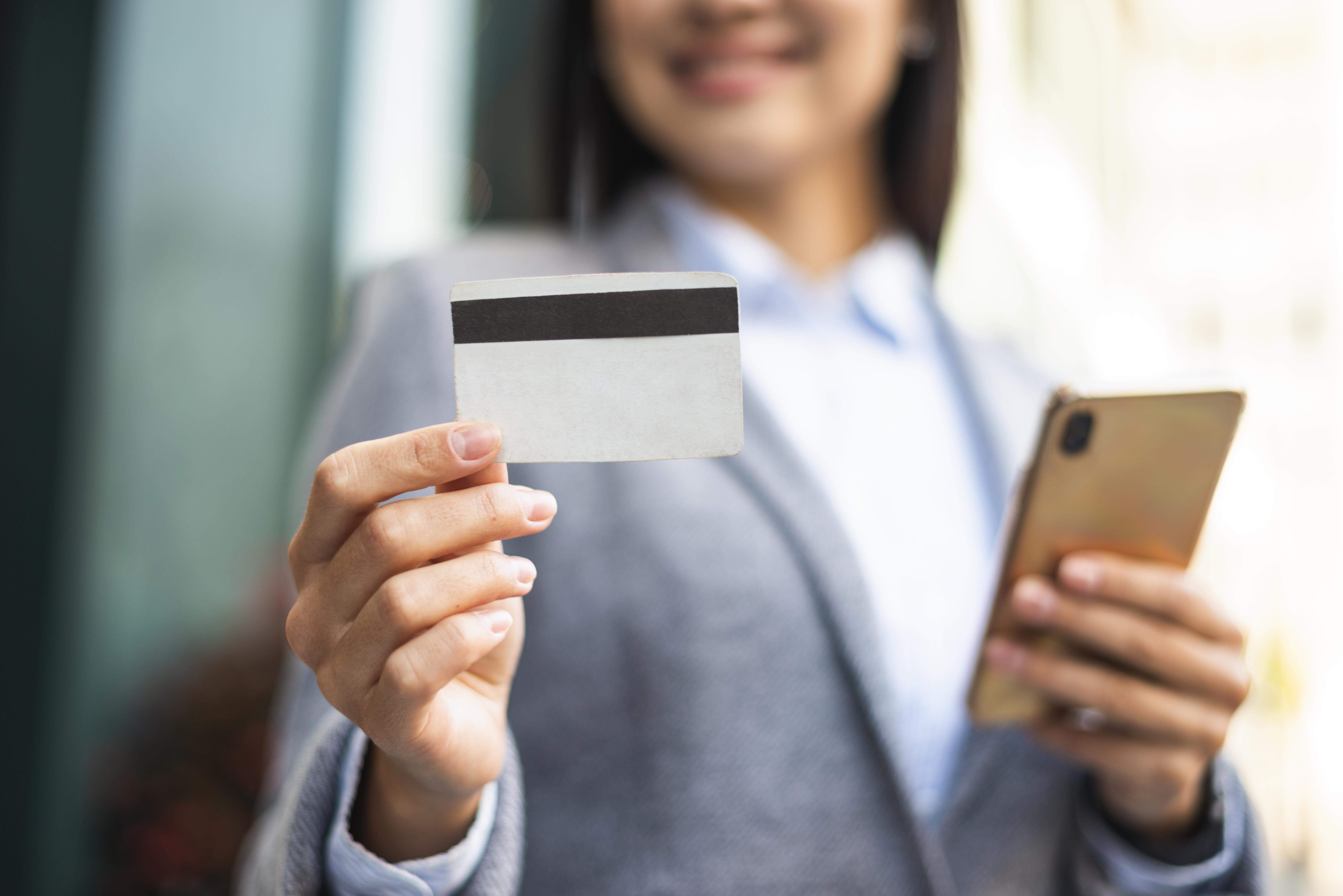 smiley businesswoman with smartphone credit card outdoors