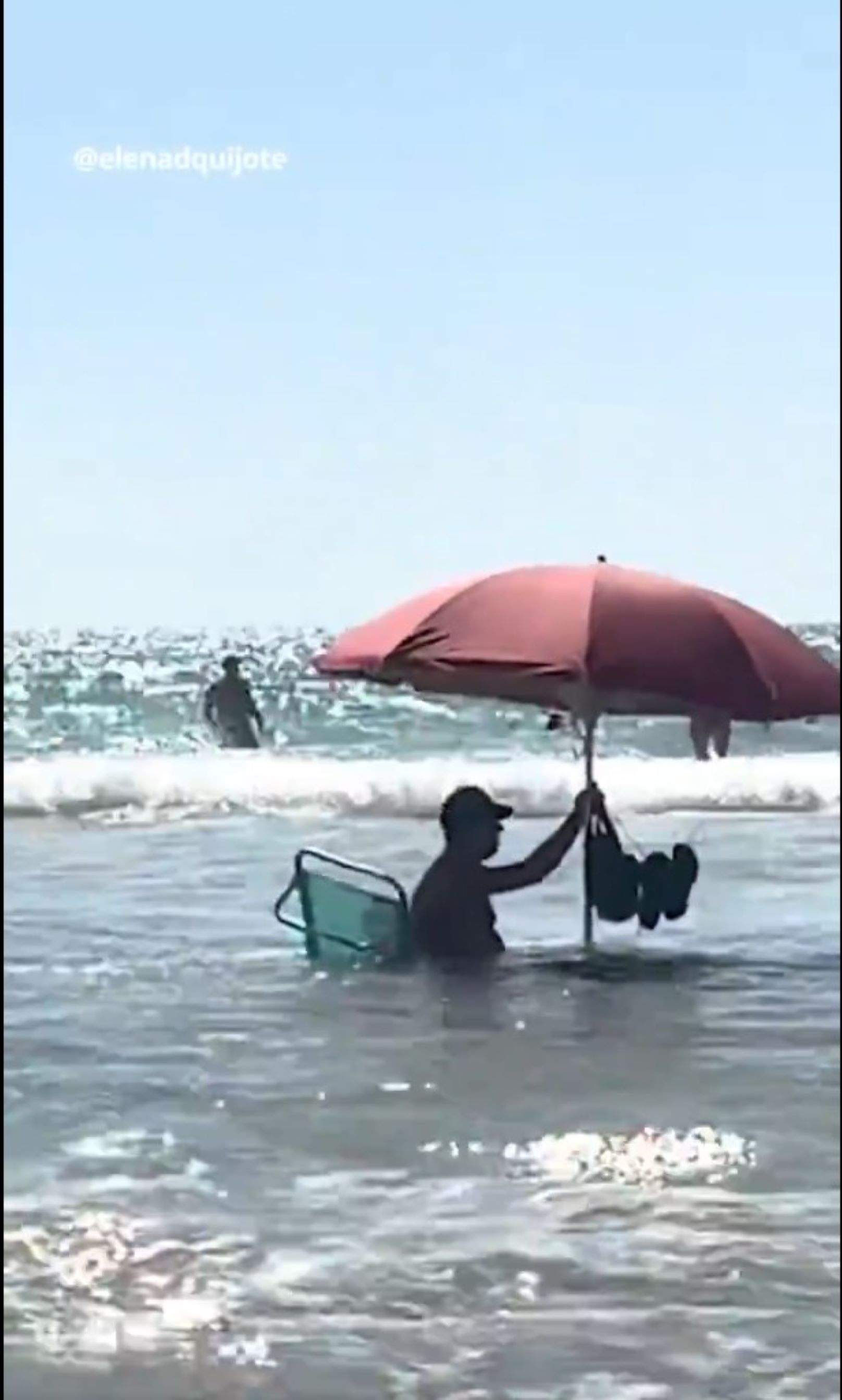 La primera línia de platja està dins l'aigua: un home s'instal·la amb el seu para-sol dins el mar